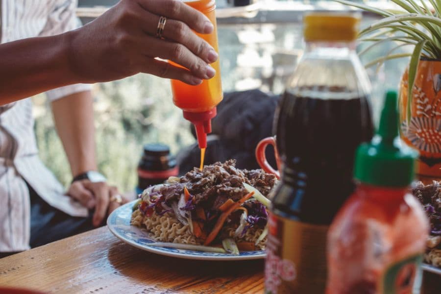 Person dispensing hot sauce in a squeeze bottle onto food