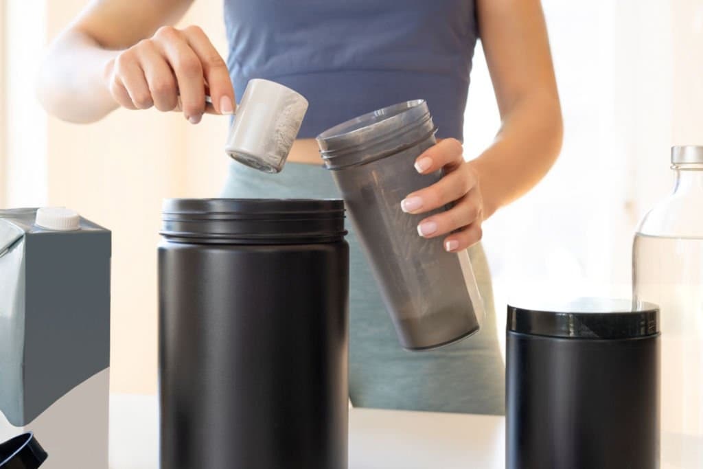 person scoops a powder supplement from container into blender cup.
